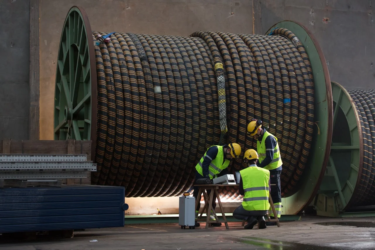 three people monitor subsea power cable on big reel with fiber optic technology